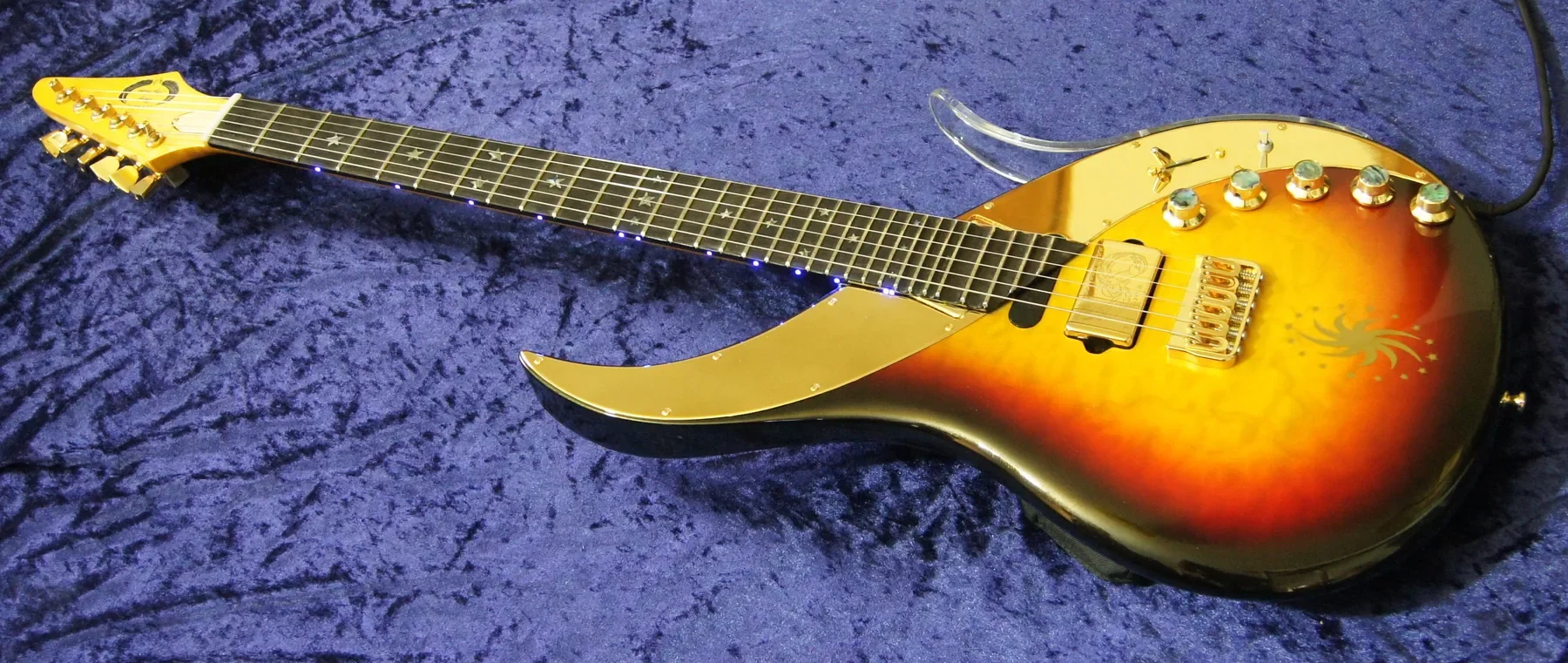 Ebony Sky sunburst sobre terciopelo azul, con diapasón de ébano y golpeador dorado en media luna