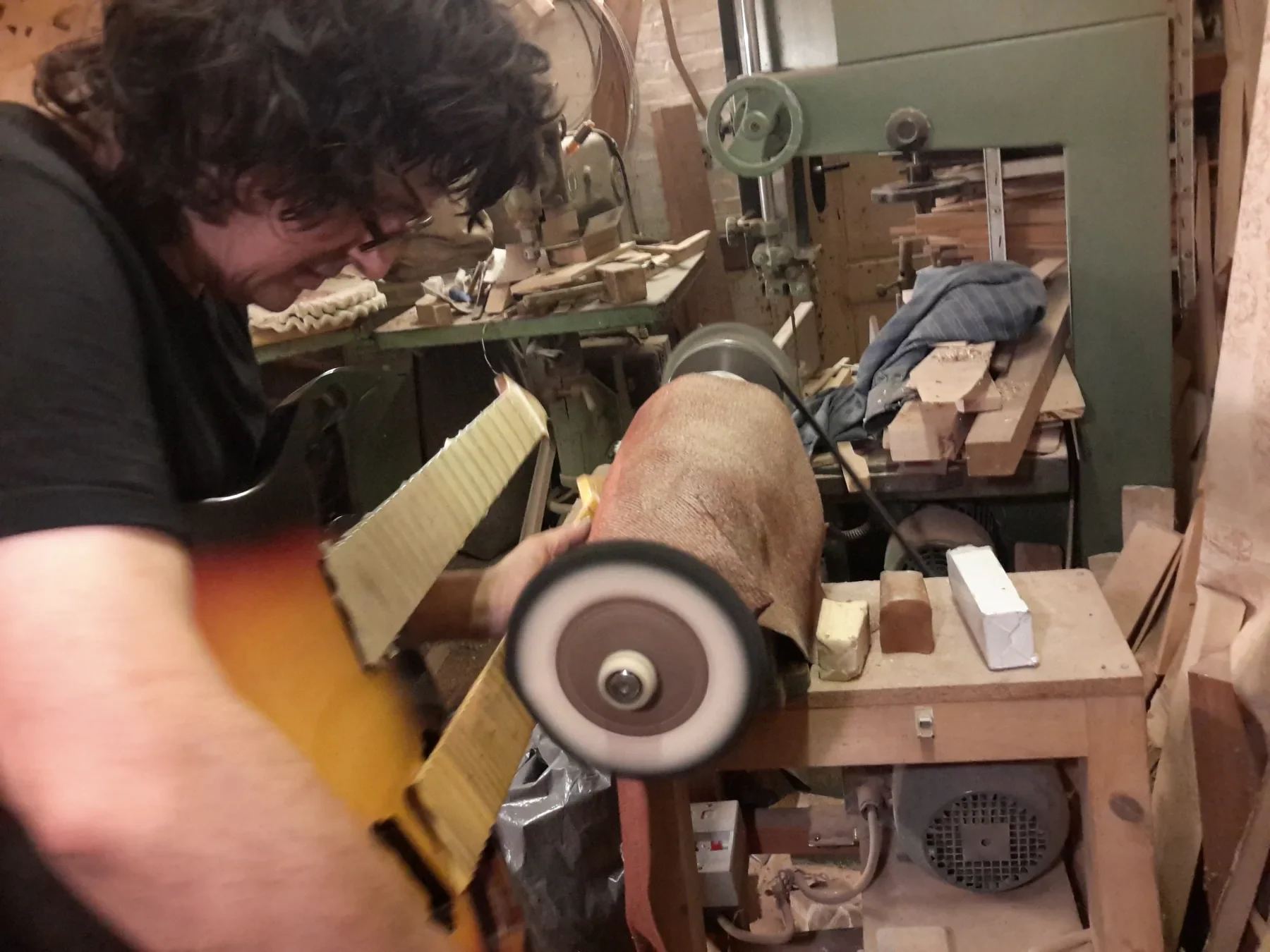 Un luthier lija un mástil en una máquina del taller, rodeado de herramientas y virutas