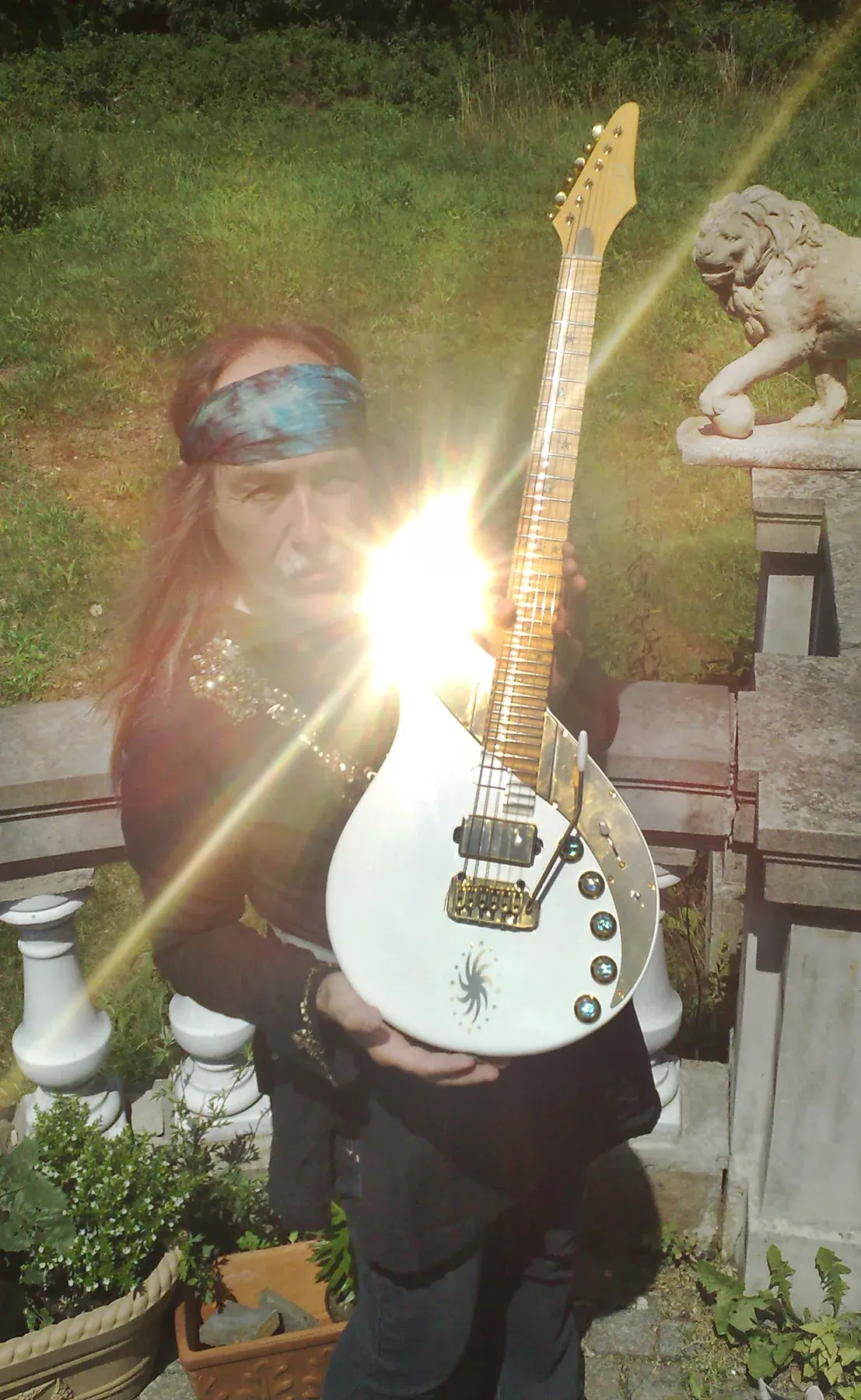 Uli Jon Roth sostiene una Bianca Sky blanca en un jardín, con un destello de sol sobre el cuerpo