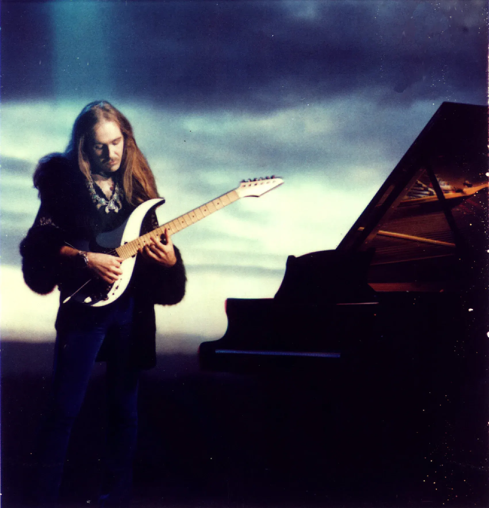 Uli Jon Roth toca la Dolphin Sky junto a un piano de cola bajo un cielo nublado, en 1985