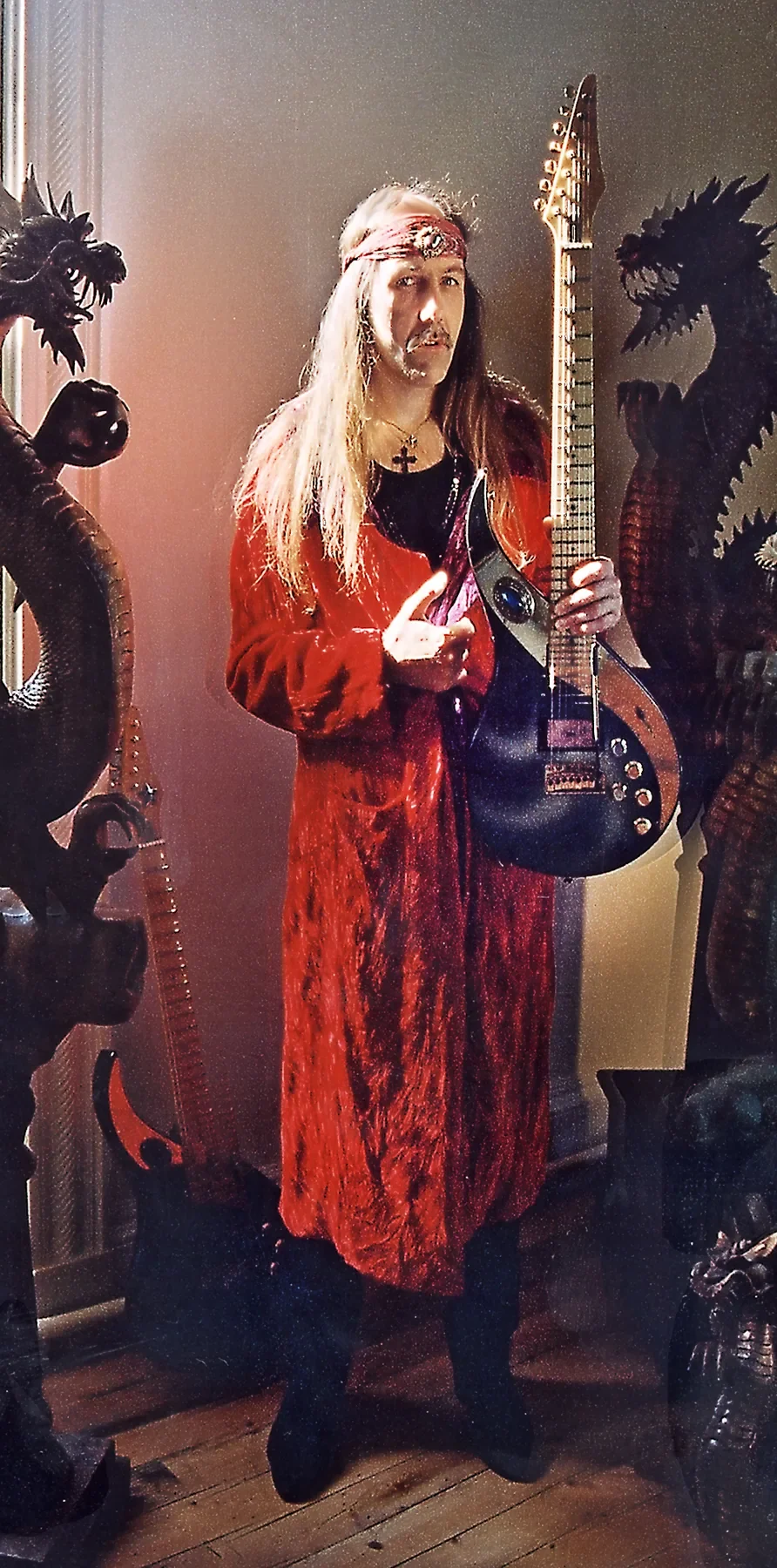 Uli Jon Roth con abrigo rojo sostiene la Rembrandt Sky entre dos esculturas de dragones