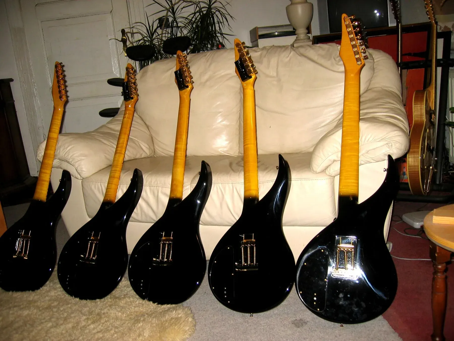 Traseras negras de cinco Sky Guitars del mismo lote, alineadas frente a un sofá