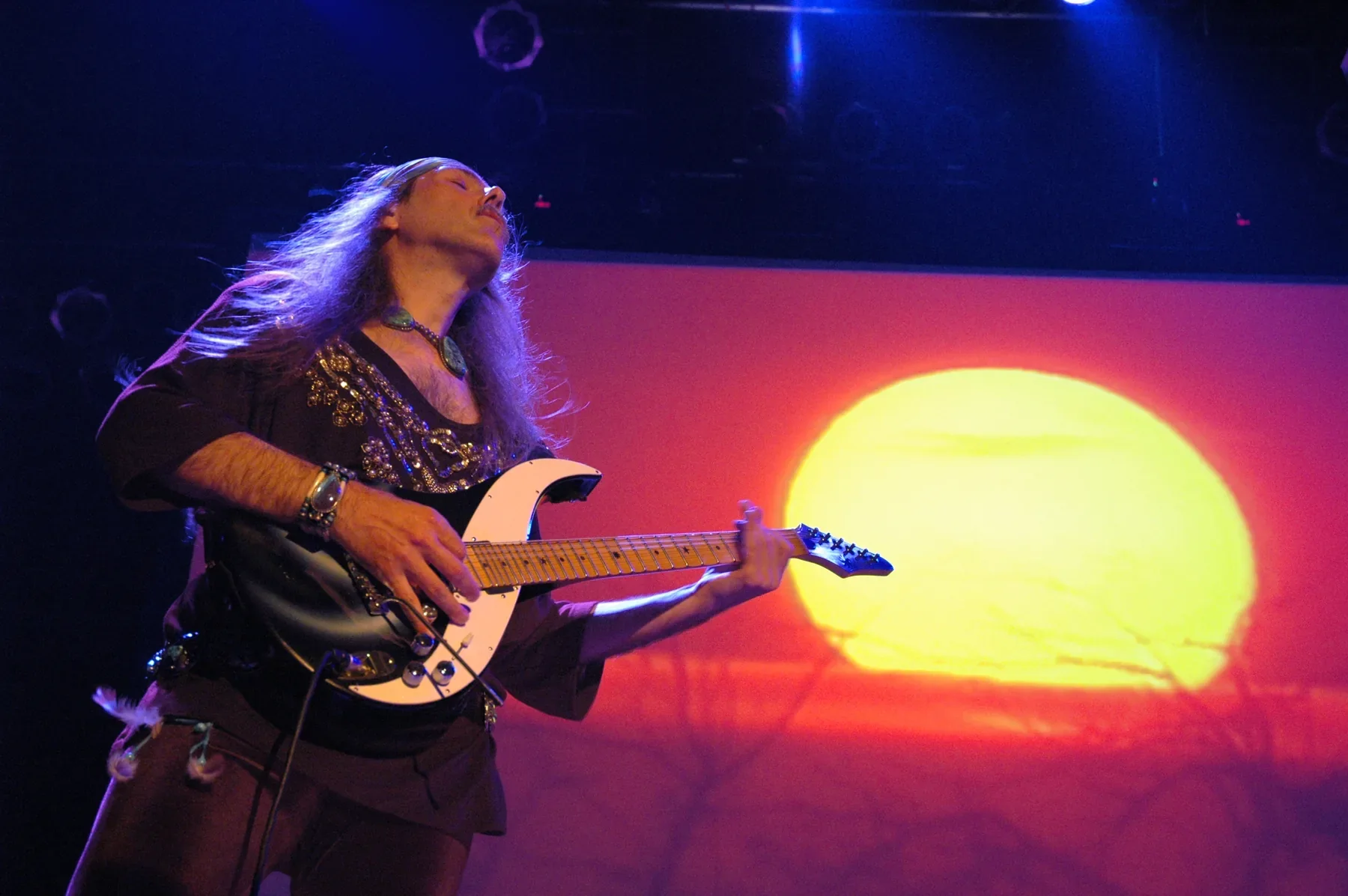Uli Jon Roth toca una Sky Guitar de cuerno blanco ante una gran proyección de un sol poniente
