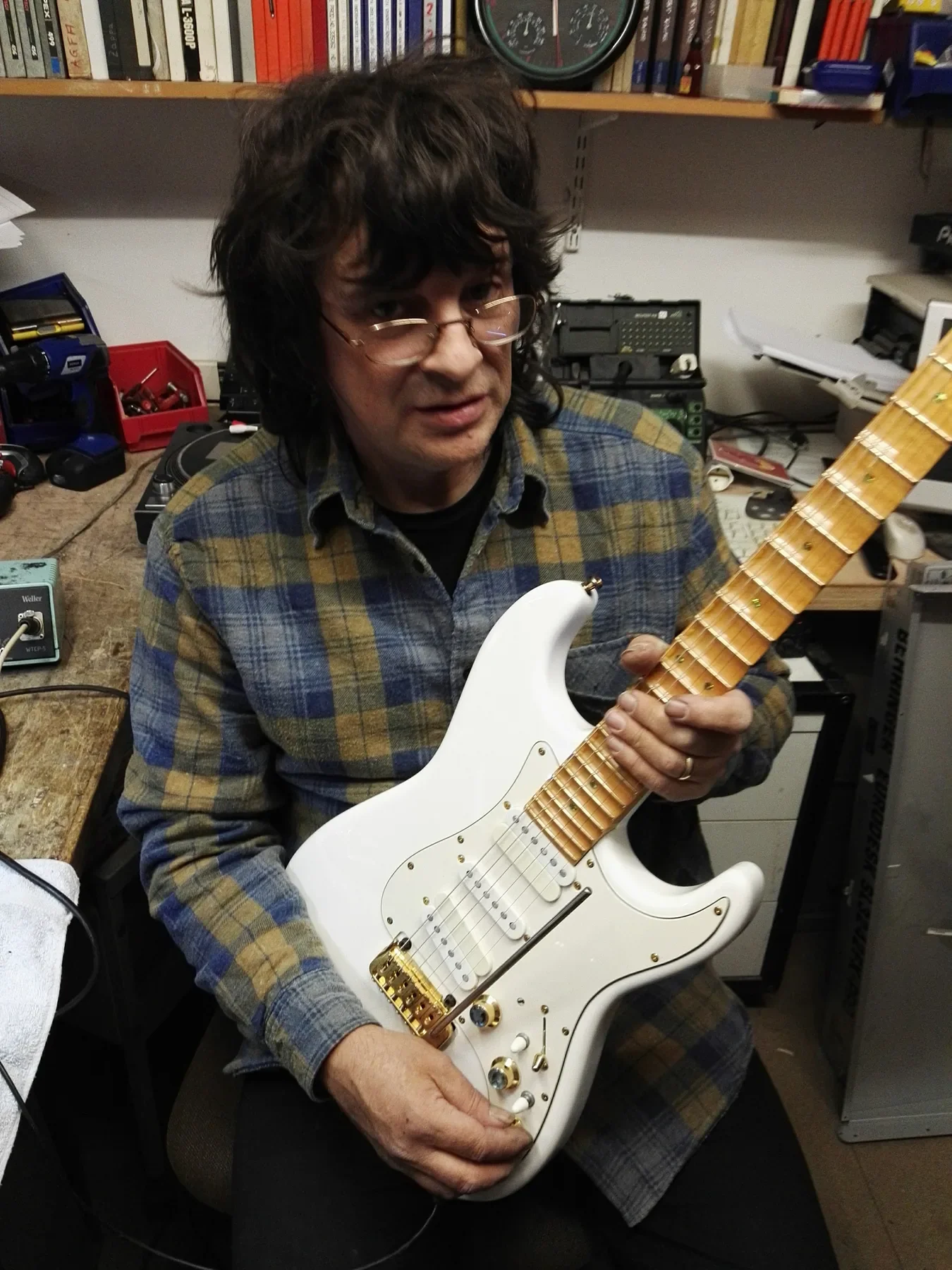 Un luthier sostiene la Sky Strat blanca junto a su banco de trabajo en el taller