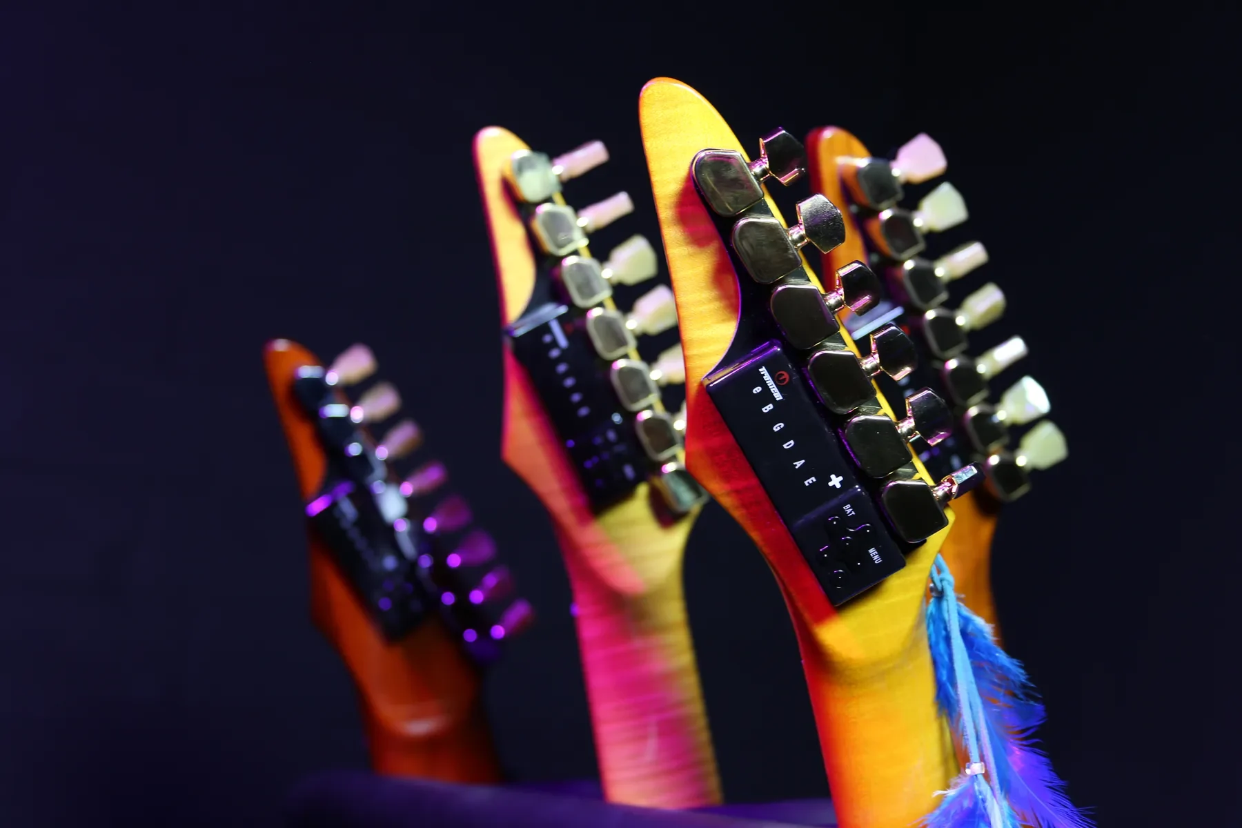 Palas de cuatro Sky Guitars con afinadores robóticos y LED, sobre fondo oscuro