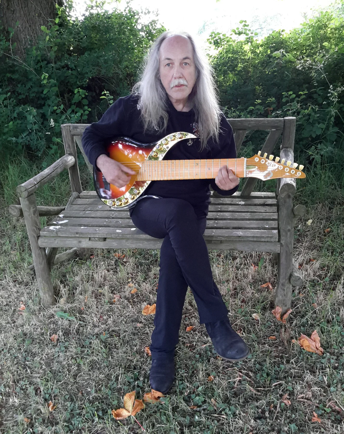 Uli Jon Roth sentado en un banco de jardín con una Sunset Sky sunburst sobre las rodillas