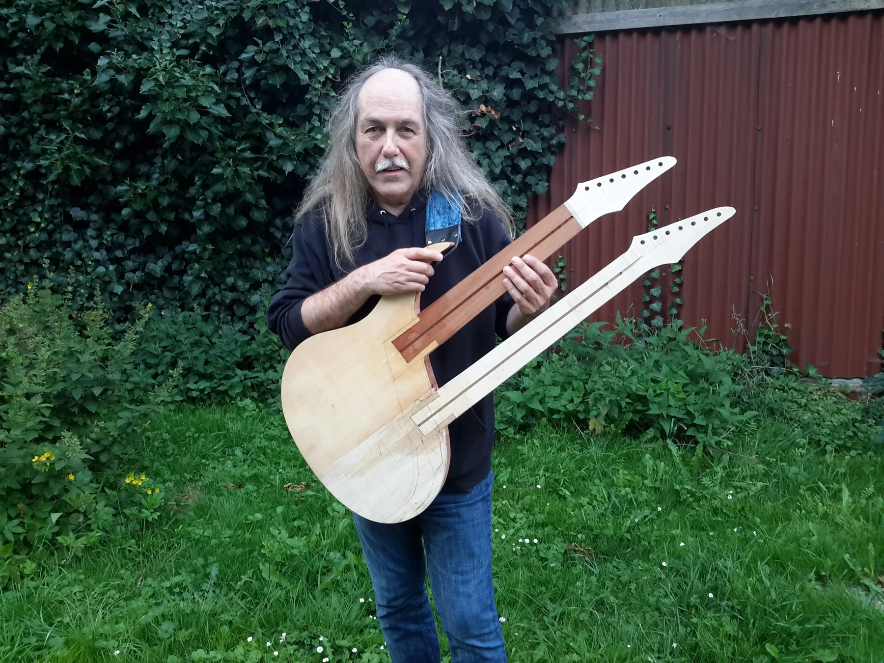 Uli Jon Roth en un jardín sostiene la doble mástil New Dawn aún sin acabar, en madera natural