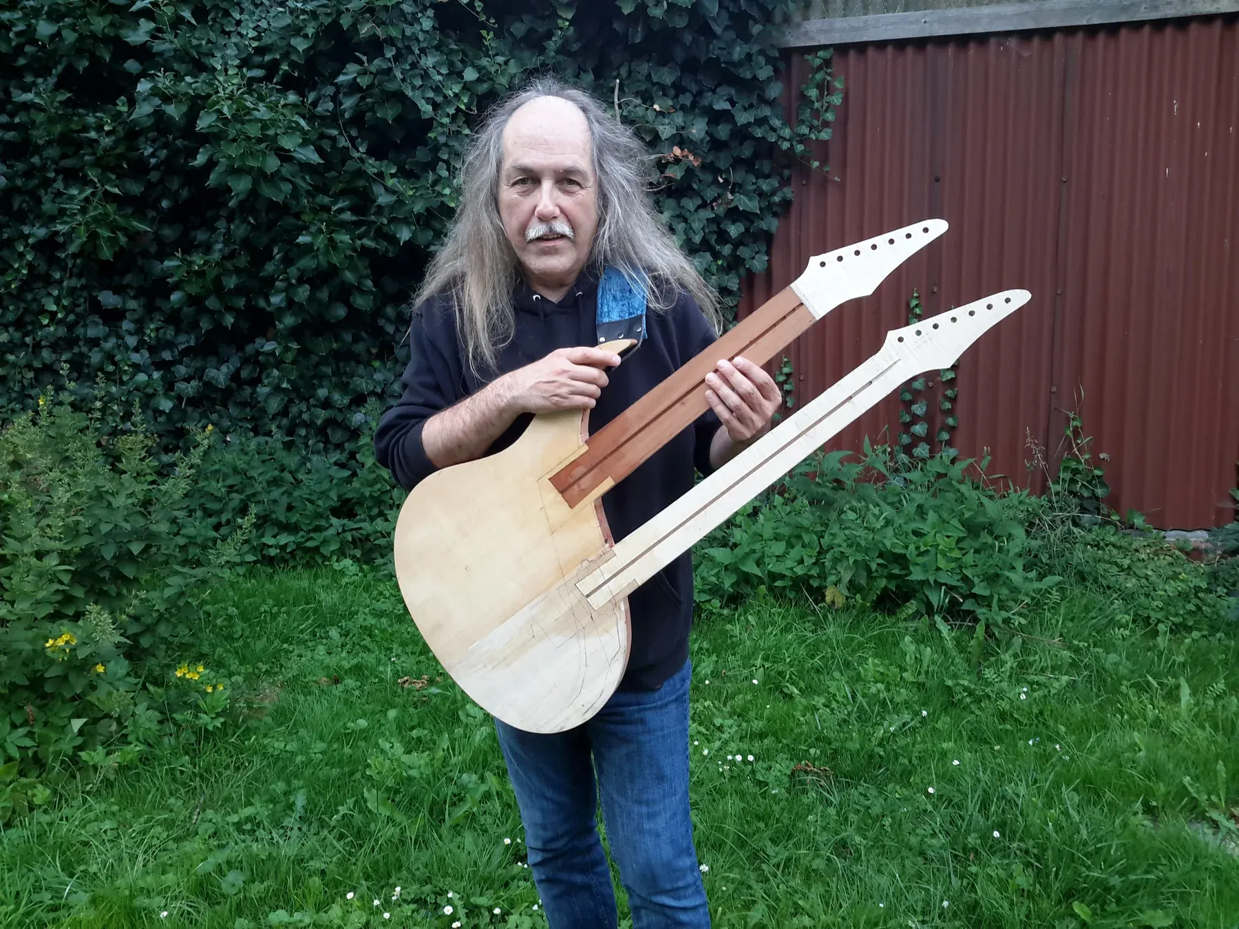 Uli Jon Roth en un jardín sostiene la doble mástil New Dawn aún sin acabar, en madera natural