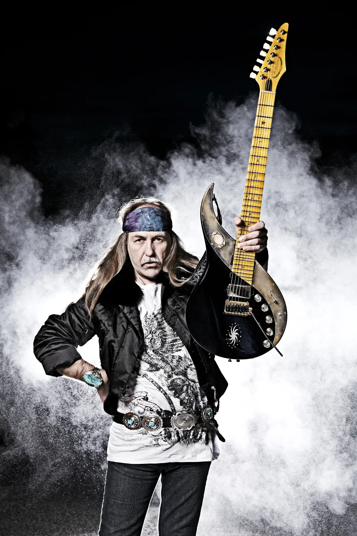 Uli Jon Roth posa entre humo blanco sosteniendo la Infinity Sky negra y dorada