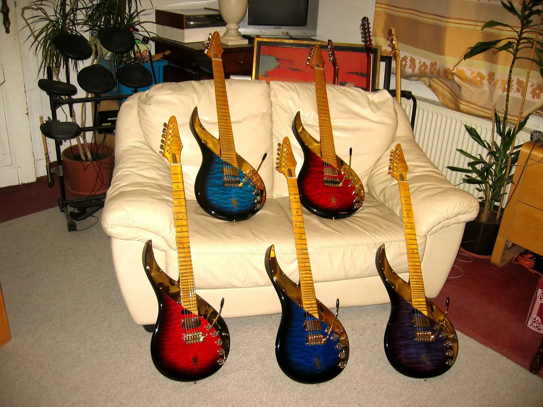 Seis Sky Guitars de un mismo lote en rojo, azul y morado, sobre y ante un sofá blanco