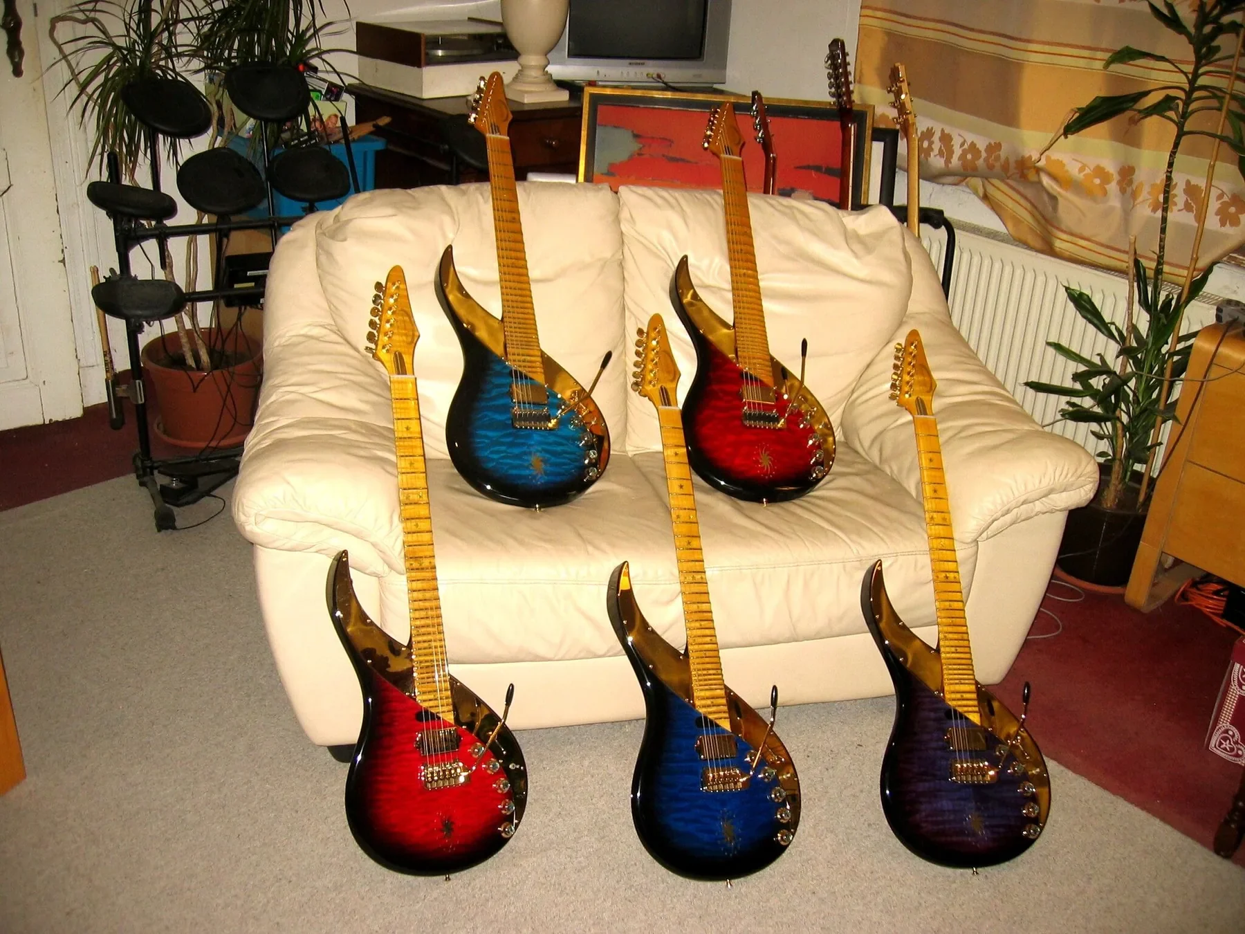 Seis Sky Guitars de un mismo lote en rojo, azul y morado, sobre y ante un sofá blanco