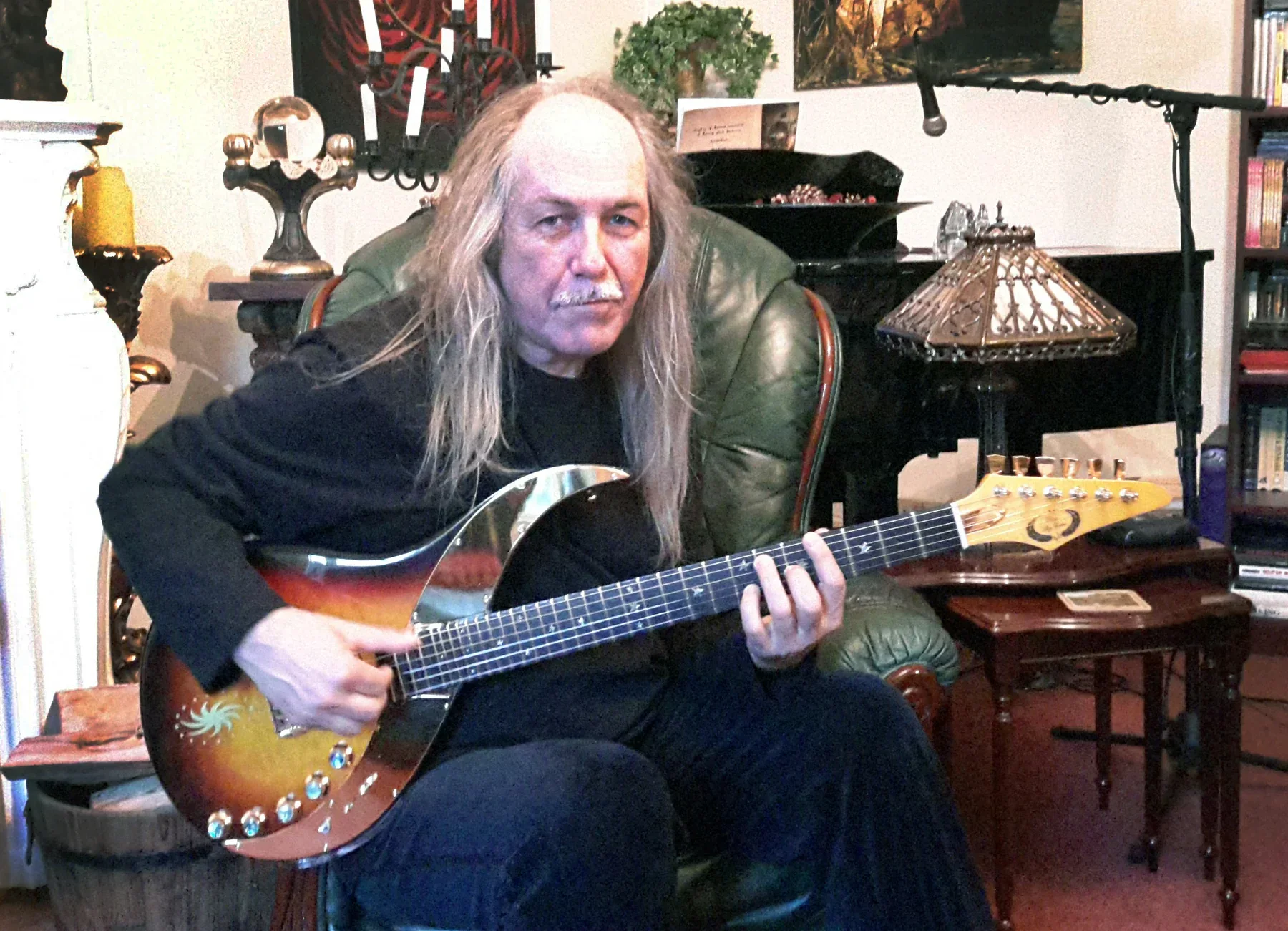 Uli Jon Roth sentado en un sillón de su casa tocando una Sky Guitar sunburst, en 2018